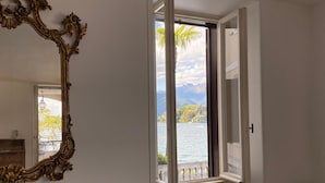 A room with a large ornate mirror, a window with a view of a lake and mountains, and a radiator below the window. - Wonderful Stresa apartment on the lake in Stresa (Stresa)