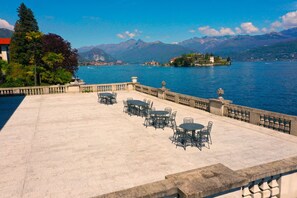 Eine Terrasse mit Sitzgelegenheiten im Freien mit Blick auf einen See, umgeben von Bergen und einer kleinen Insel mit Gebäuden.
