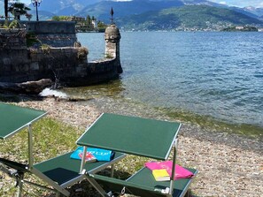 Blick auf einen See mit einer Steinmauer, einem kleinen Turm und grünen Liegestühlen mit Büchern.