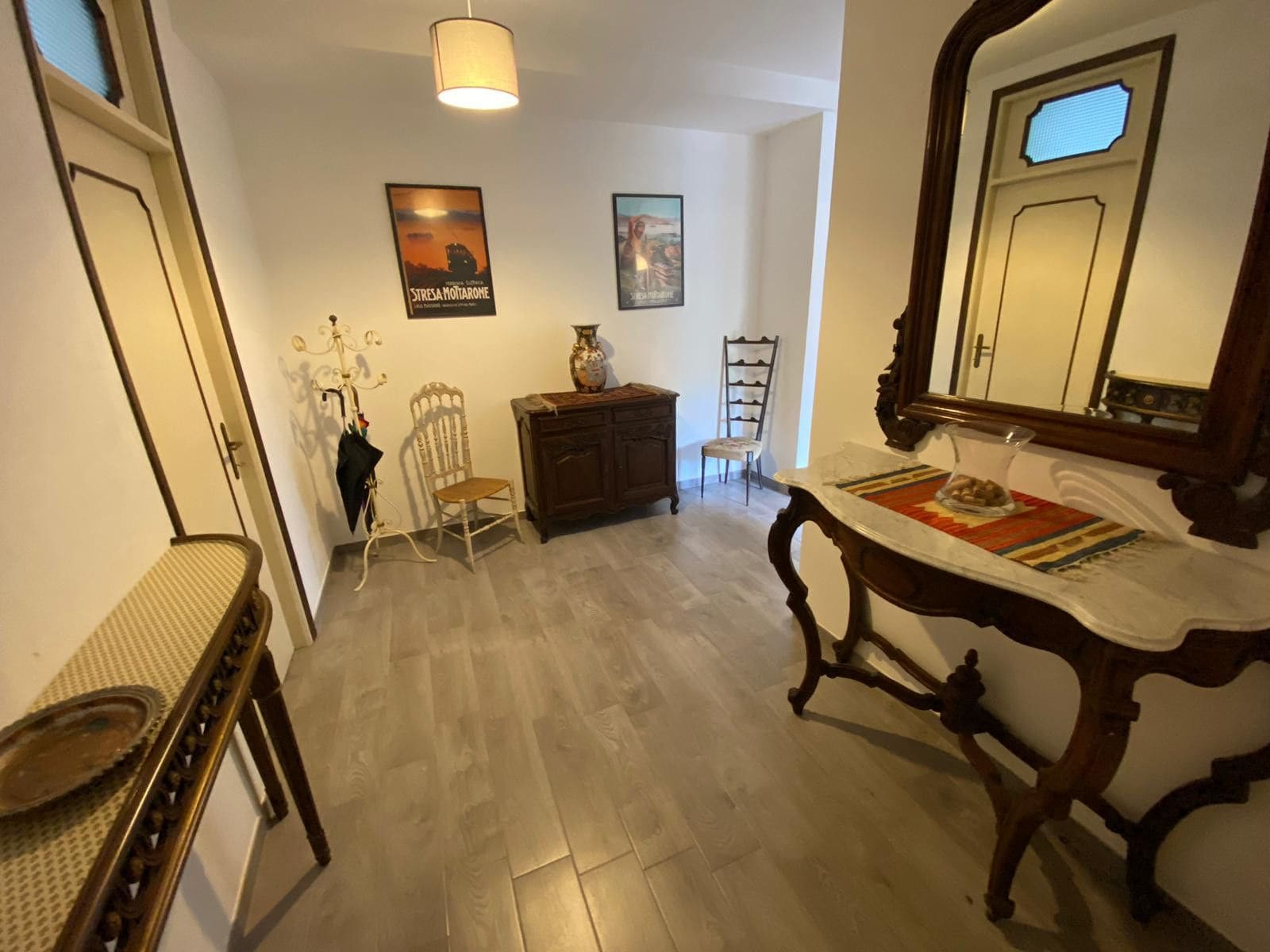 A hallway with a wooden floor, a mirror, a table with a placemat, a chair, a cabinet, and wall-mounted pictures.