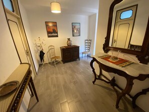 Passadís amb sòl de fusta, mirall, taula amb suport per a plats, cadira, armari i quadres penjats a la paret.