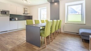 Een moderne keuken met witte kasten, een magnetron en een inbouwoven. Er is een eethoek met een tafel en groene stoelen.