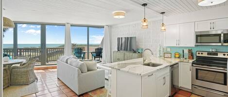 A spacious living area with a large window overlooking the sea, a kitchen with modern appliances, and a cozy seating area.