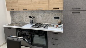 Une cuisine compacte dotée de meubles hauts en bois, d’un plan de travail blanc, d’un évier en acier inoxydable, d’une cuisinière à gaz et d’un lave-vaisselle.