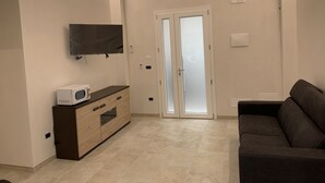 Un salon moderne avec un téléviseur à écran plat fixé au mur, un canapé de couleur foncée et un meuble en bois contenant un four à micro-ondes.