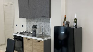 Une cuisine moderne avec des meubles gris, un réfrigérateur noir et une cuisinière à gaz.