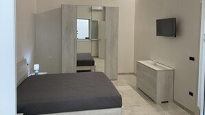 Une chambre moderne avec un lit, une coiffeuse avec un miroir, un téléviseur fixé au mur et un dressing.