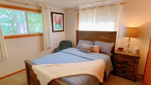 Um quarto com cama, uma cadeira, mesa de cabeceira com abajur e um quadro na parede.