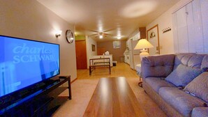 Sala de estar com televisão, ventilador de teto, sofá, mesa de jantar e cozinha ao fundo.