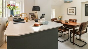 Una cucina moderna con isola centrale, zona pranzo con tavolo e sedie in legno e un'ampia finestra che offre luce naturale.