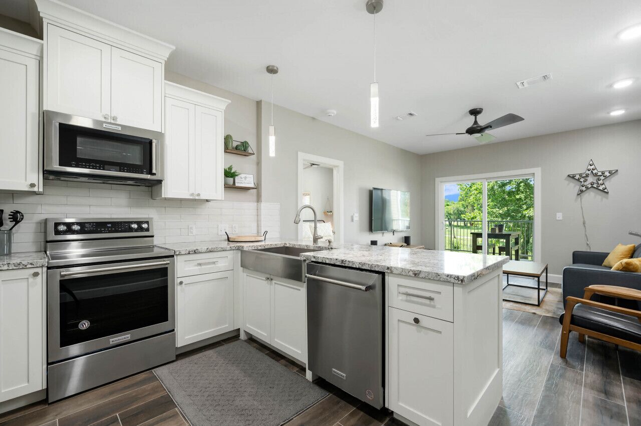 A modern kitchen with white cabinets, stainless steel appliances, a dishwasher, and a dining area with a gray sofa and wooden bench.