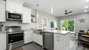 A modern kitchen with white cabinets, stainless steel appliances, a dishwasher, and a dining area with a gray sofa and wooden bench.