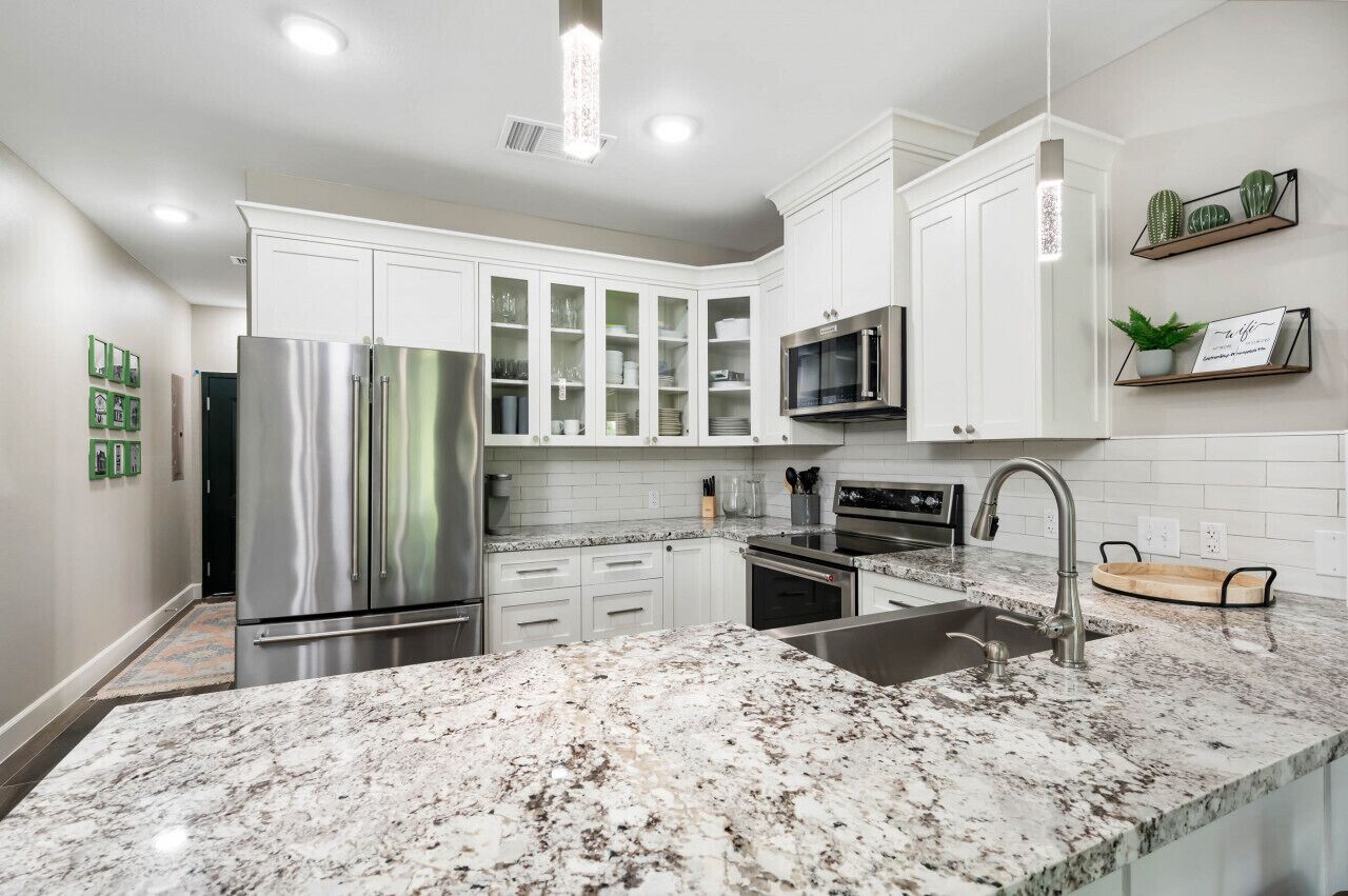 A modern kitchen with white cabinets, stainless steel appliances, a granite countertop, and a microwave.