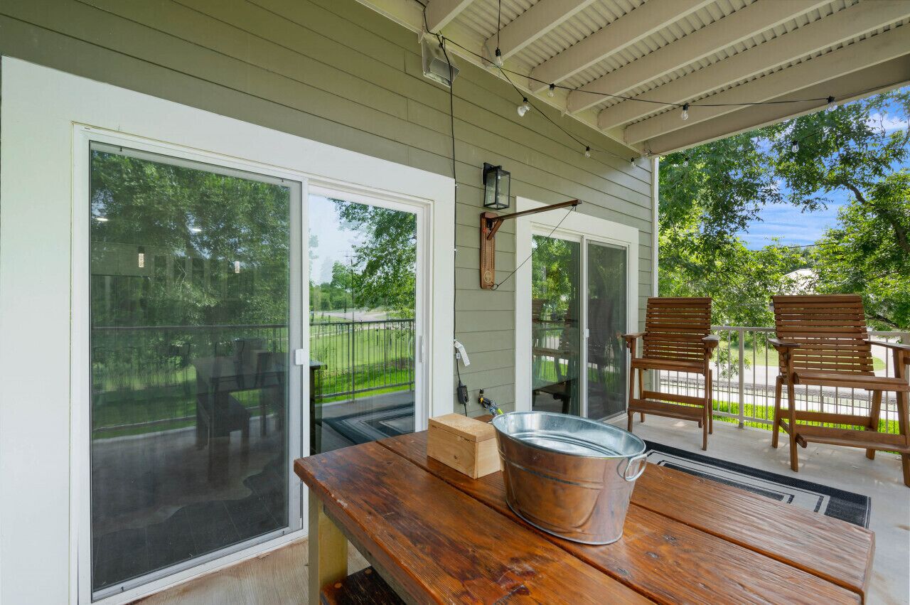 A covered patio with a wooden table, a metal bucket, and two wooden chairs.