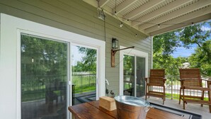 Une terrasse couverte avec une table en bois, un seau en métal et deux chaises en bois.