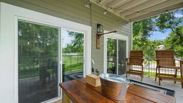 A covered patio with a wooden table, a metal bucket, and two wooden chairs.