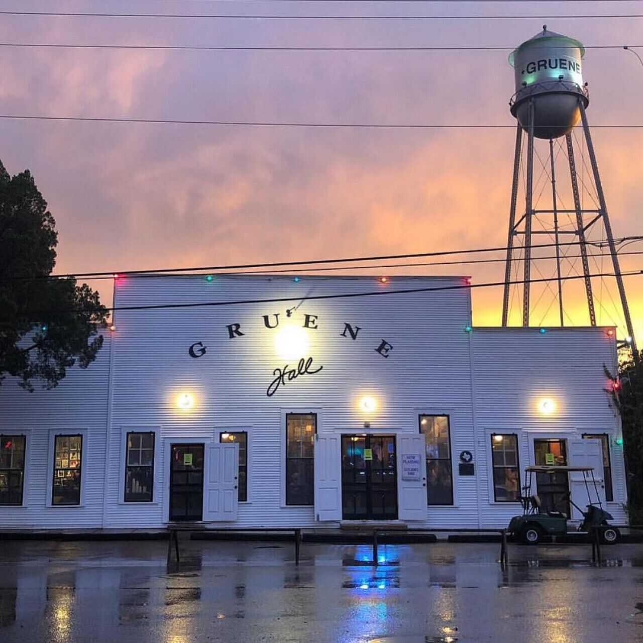 A building with 'GRUENE Hall' signage, a water tower, and a wet ground reflecting lights.