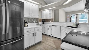 Une cuisine moderne avec des meubles blancs, des appareils en acier inoxydable et un grand îlot central.