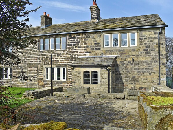 A stone building with multiple windows, a chimney, and a stone pathway leading to the entrance.