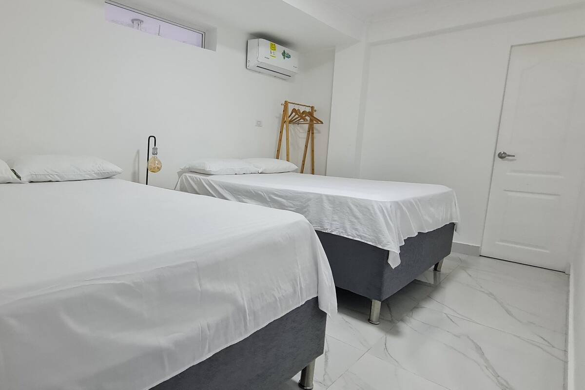 A hotel room with two beds, a wall-mounted air conditioner, a wooden hanger rack, and a door.
