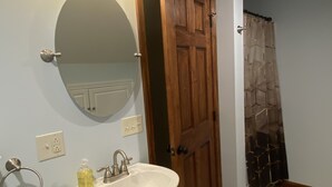 Un baño con un lavamanos pedestal, un espejo y una puerta de madera.
