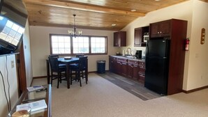 Una cocina amplia con armarios de madera, un refrigerador negro y un comedor con mesa y sillas.
