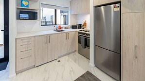 A modern kitchen with light wood cabinets, a stainless steel refrigerator, a microwave, and a coffee maker.