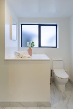 Un baño con tocador blanco, inodoro y ventana con vidrio esmerilado.