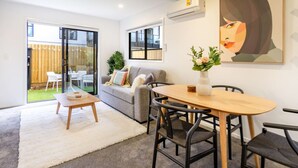 A modern living room with a sofa, a dining table with chairs, a white rug, and a large window.
