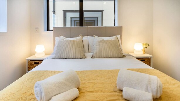 A hotel room with a bed, two bedside lamps, and a window.