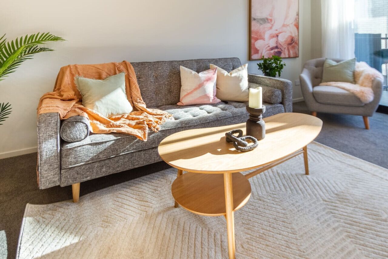 A living room with a grey sofa, a round wooden coffee table, and a beige rug.