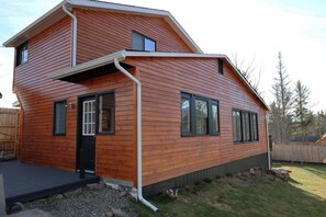 A two-story wooden house with a front porch, a small deck, and a fenced backyard.