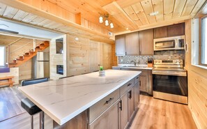 A modern kitchen with wooden cabinetry, stainless steel appliances, and a marble countertop.