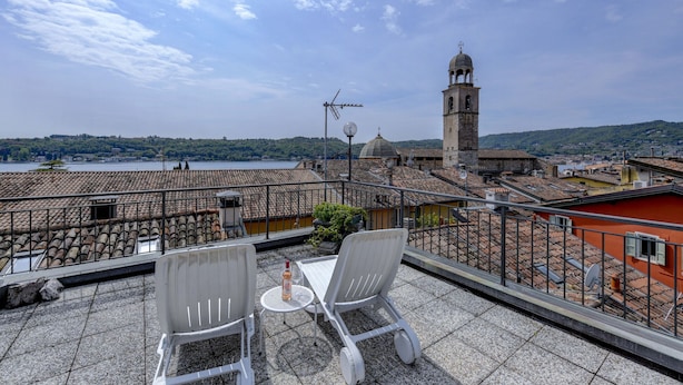 Terraza con dos sillas blancas y una mesa, con vista a un paisaje urbano que incluye una torre destacada y un cuerpo de agua.