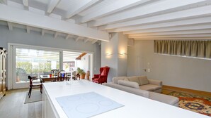 Una cocina moderna con una isla central, una zona de comedor con una silla roja y un salón con sofá y alfombra estampada.