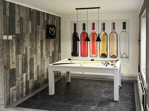 Een pooltafel met biljartballen, een houten wand met een logo en flessen wijn die aan de muur hangen.