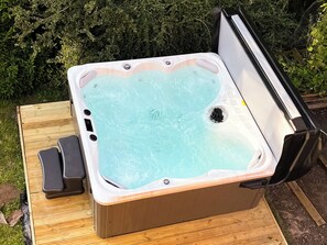 Un bain à remous doté d’une terrasse en bois, entouré de verdure.