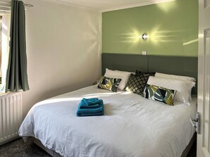 A hotel room with a bed, a window with curtains, a wall-mounted light, and a radiator.