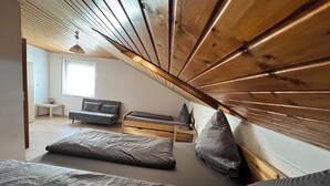 A loft bedroom with a sloped ceiling, a bed, a sofa, and a small table.