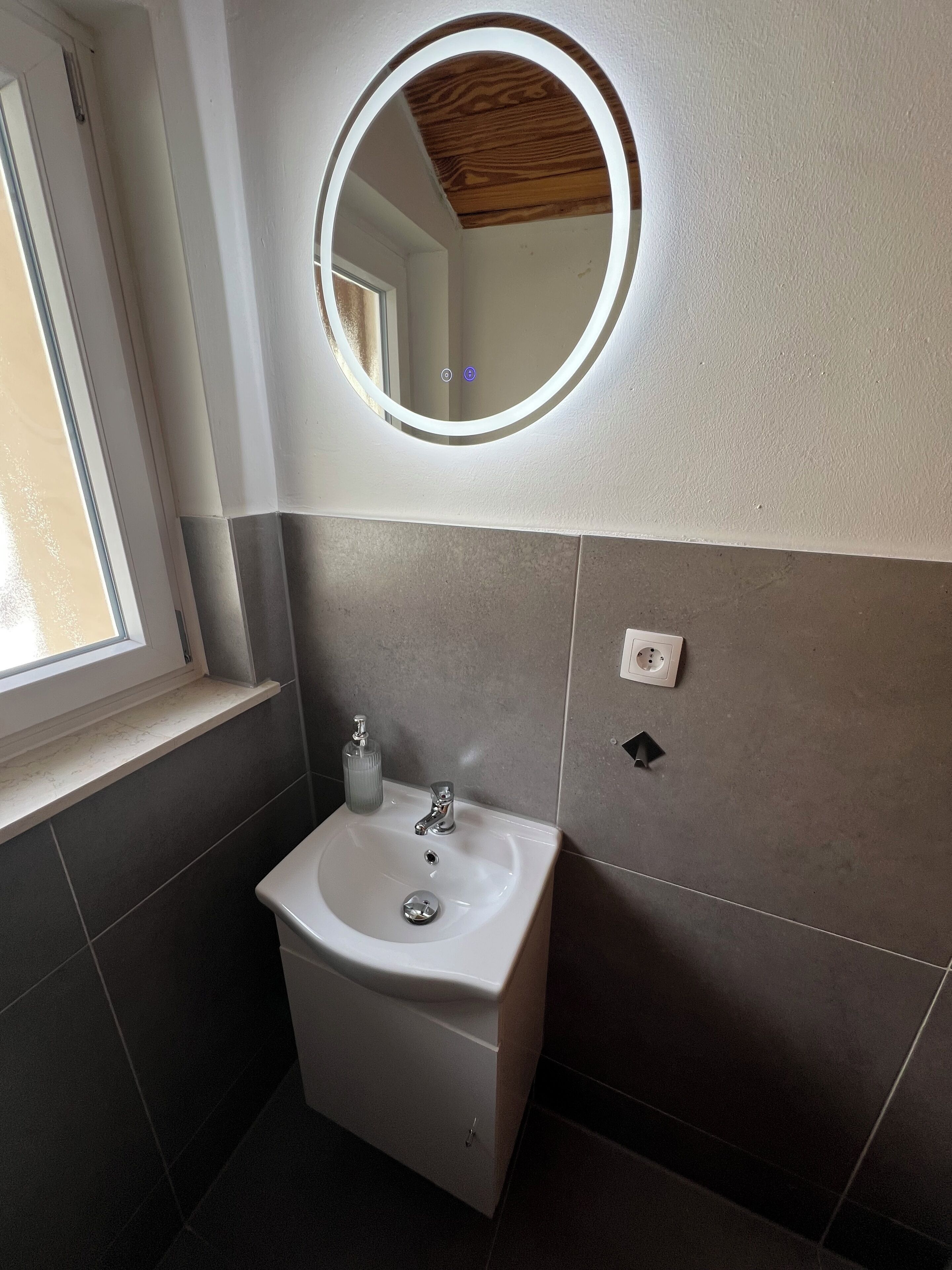 A bathroom with a white sink, a mirror with a light, and a window.