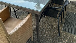 An outdoor patio with a glass-top table, wicker chairs, and a black mesh screen.