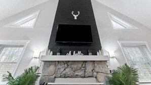 Un salon moderne avec une cheminée, un téléviseur fixé au mur et un mur d’accent en pierre.