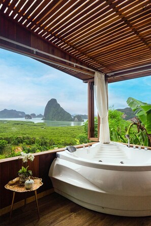 A hot tub in a room with a wooden ceiling and a view of a lush landscape with mountains and water.
