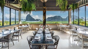Een restaurant met een lange tafel gedekt voor diners, omringd door stoelen, met uitzicht op bergen en groen door grote ramen.