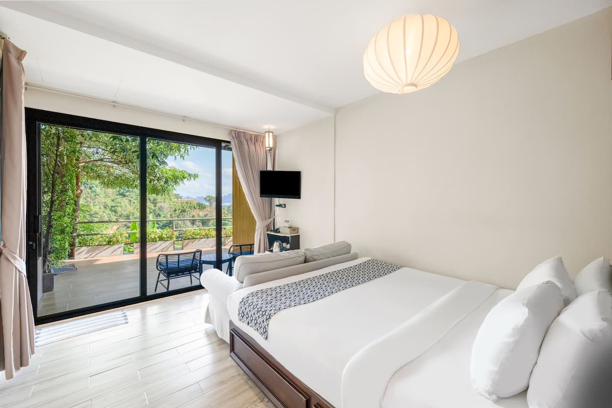 Een slaapkamer met een groot bed, een televisie, een plafondlamp en uitzicht op een balkon met een stoel en tafel.