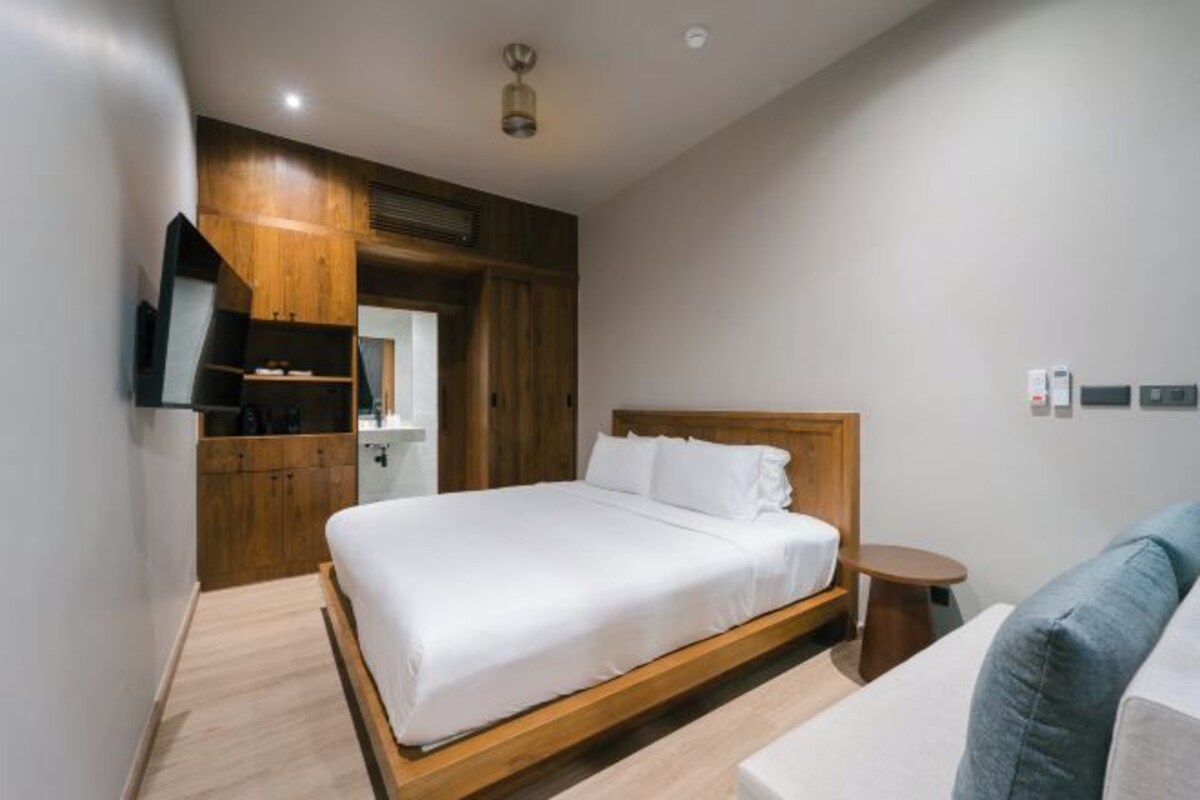 A modern bedroom with a wooden bed frame, a small bedside table, and a built-in TV.