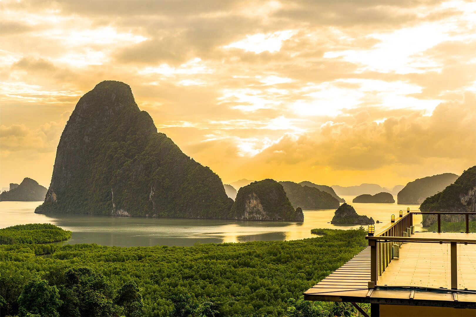 A coastal landscape with a prominent limestone peak, a wooden viewing platform, and lush greenery.