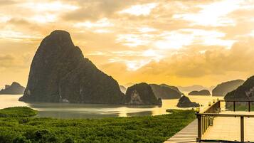 A coastal landscape with a prominent limestone peak, a wooden viewing platform, and lush greenery.