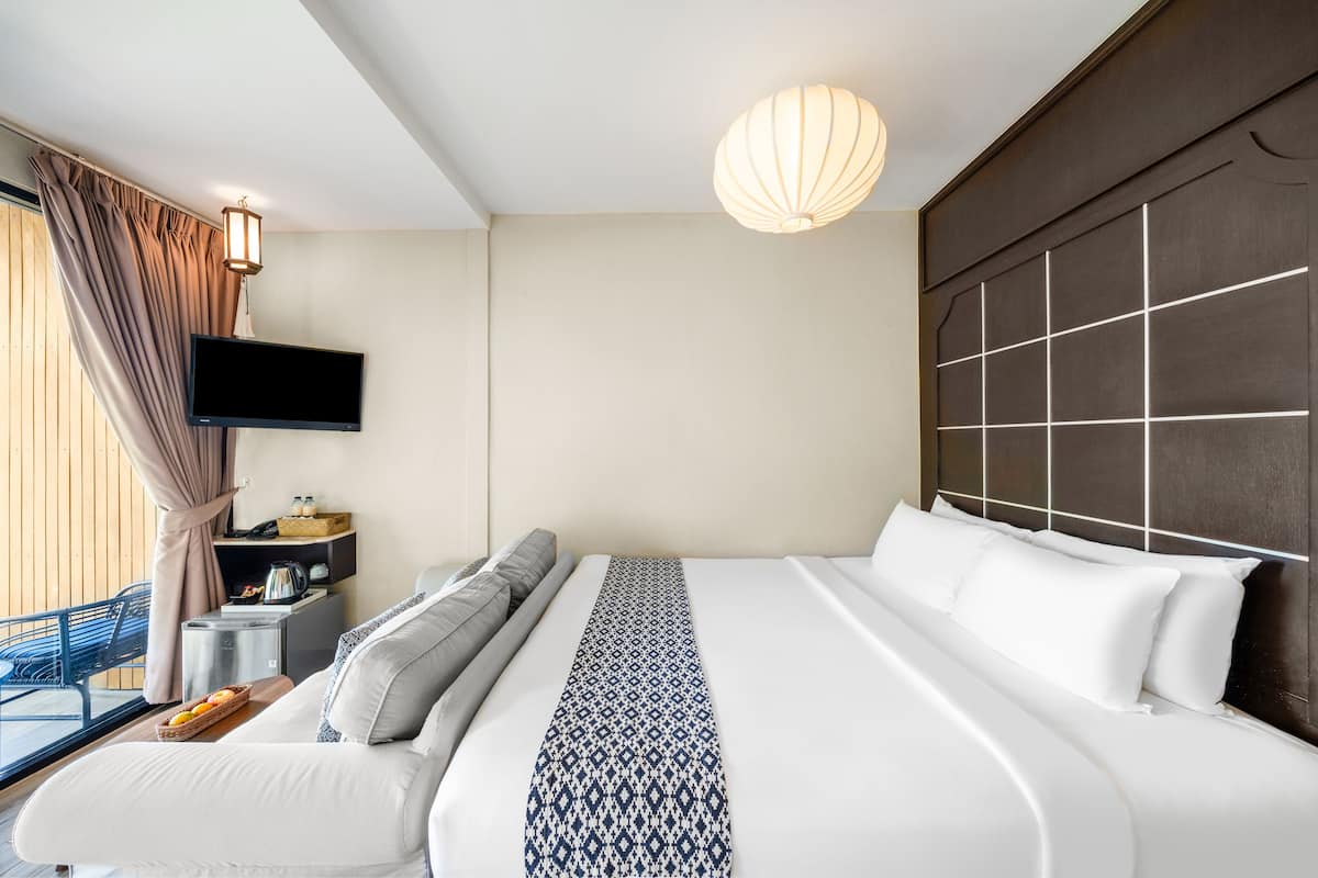 Een moderne hotelkamer met een groot bed, een flatscreen televisie aan de wand, een nachtkastje met een lamp, en uitzicht op de omgeving door grote ramen.
