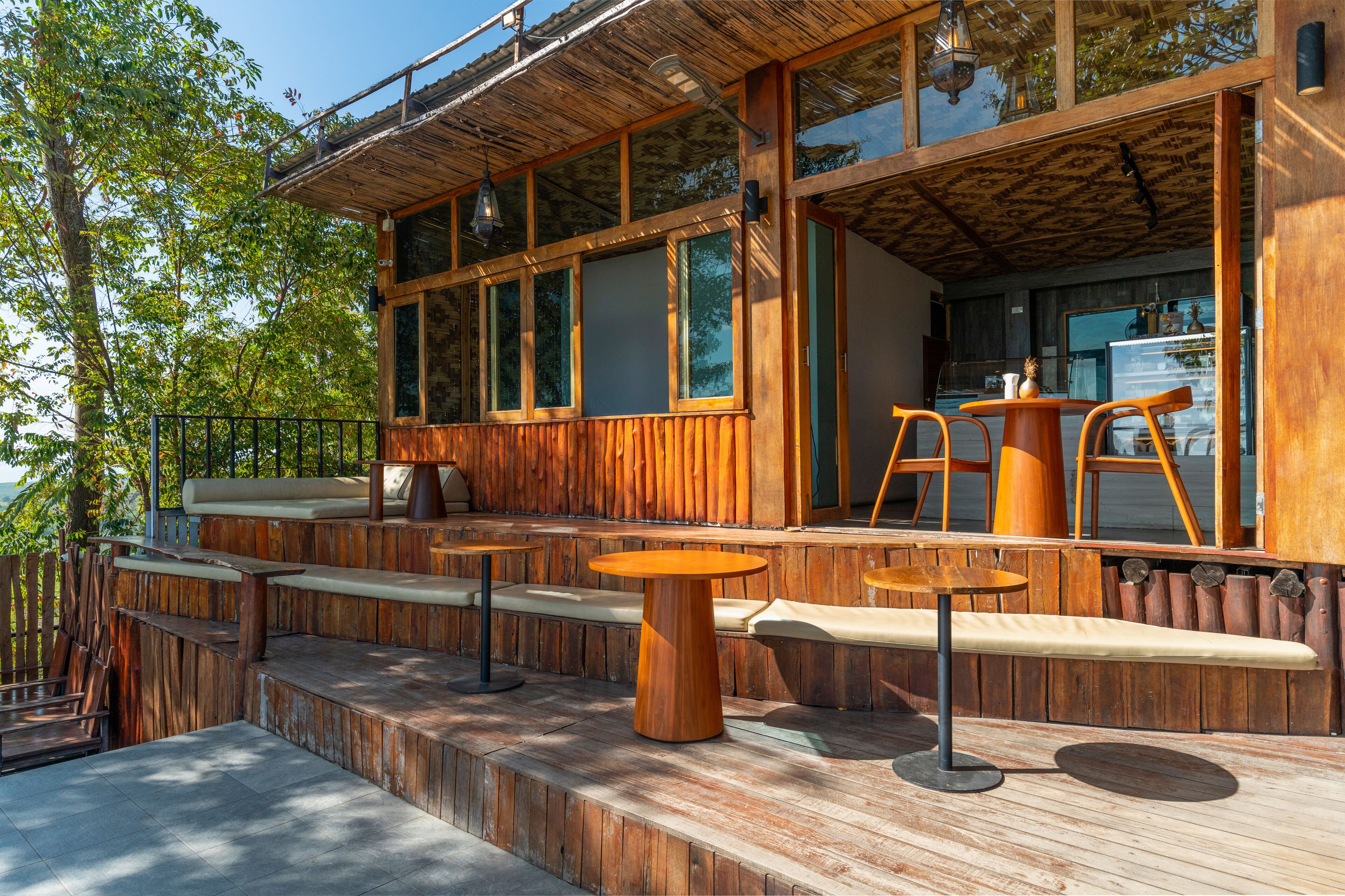Una terraza de madera con mobiliario exterior, ventanas amplias y vistas a los árboles circundantes.